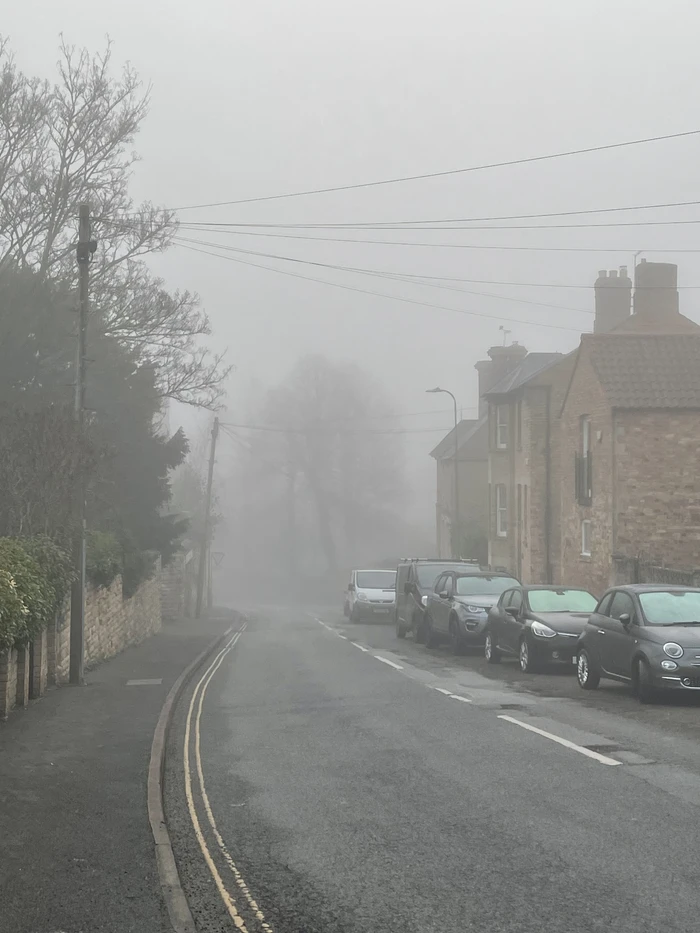 Looking downhill along an empty road in a misty Stamford